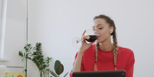 Mulher toma vinho enquanto observa a tela de um computador.