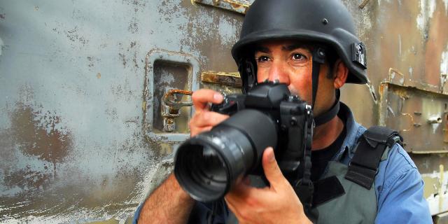 Jornalista utilizando capacete e colete de proteção com câmera na mão