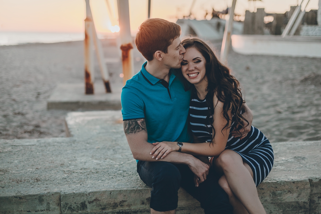 Homem beijando cabeça da  mulher enquanto ela sorri na praia
