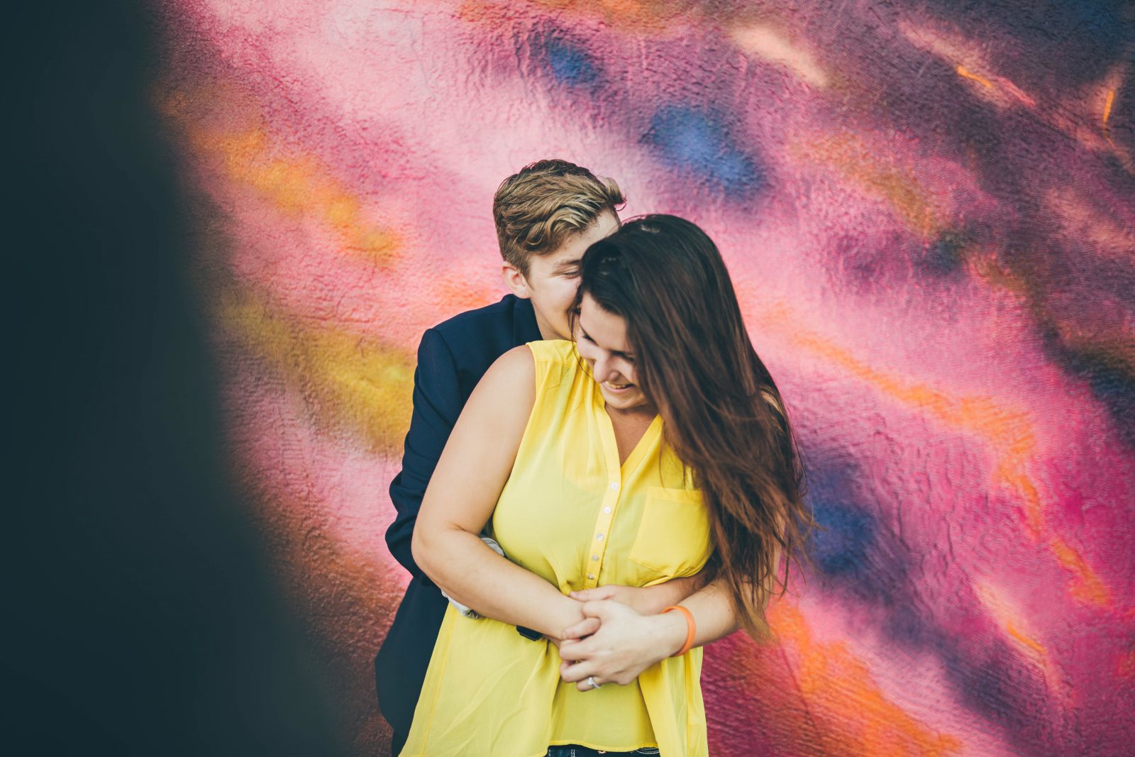 Casal se abraçando de frente para um muro colorido