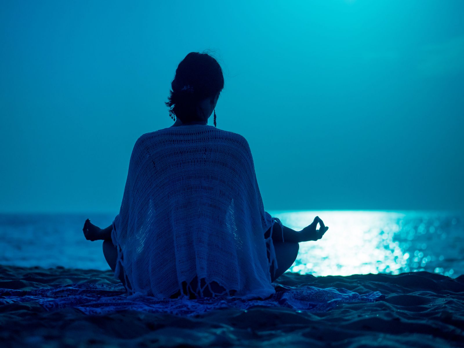 Mulher meditando em frente ao mar com a luz da lua