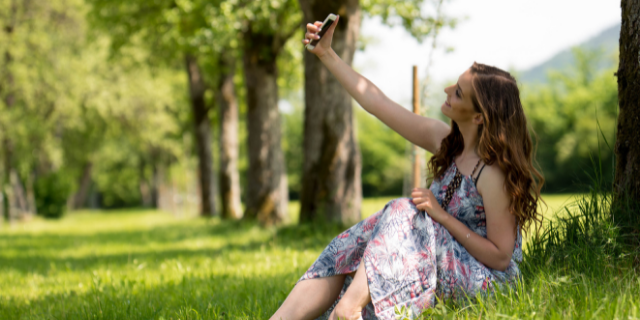 Mulher tirando selfie no parque sentada na grama