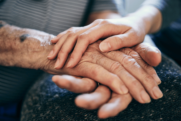 Mãos de uma jovem sobre a mão de uma senhora idosa, em demonstração de afeto. 