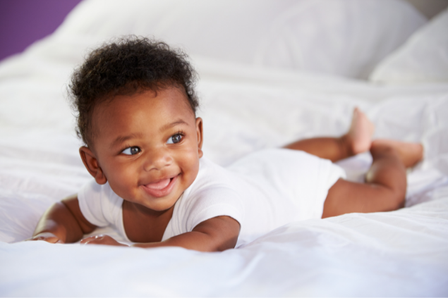 Bebê sorrindo enquanto está deitado de bruços na cama