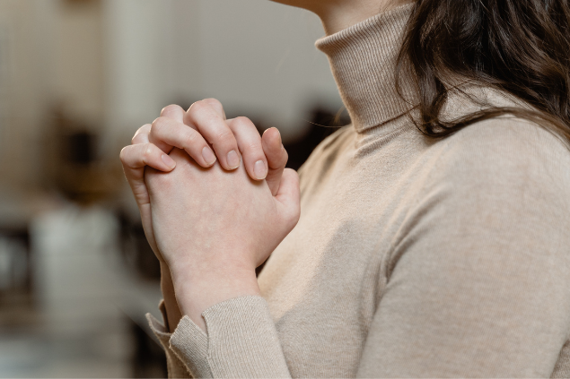 Mulher com as mãos fechadas orando