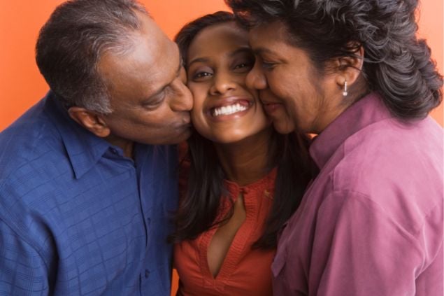 Imagem dos pais beijando a filha no rosto
