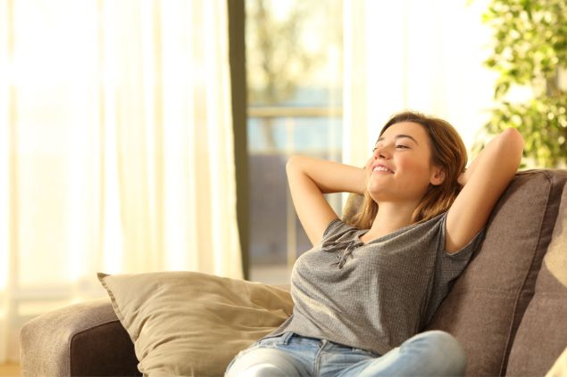 Imagem de uma mulher sentada no sofá de casa bem confortável