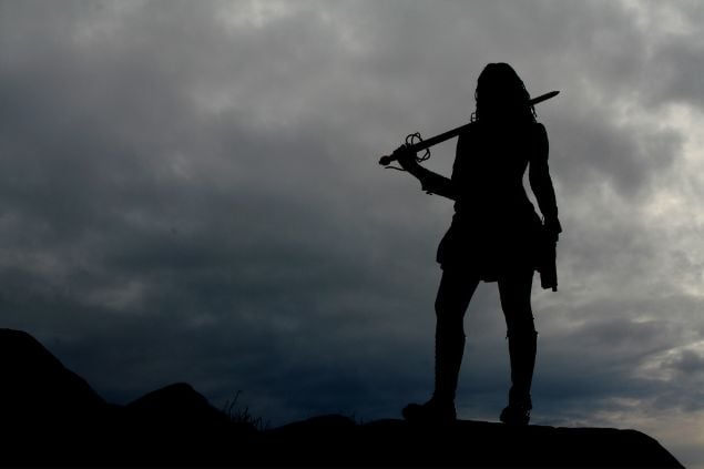 Imagem de uma guerreira no topo de uma montanha, não é possível ver seu rosto, apenas sua silhueta