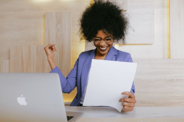 Imagem de uma mulher no escritório, sorrido e comemorando ao olhar um papel