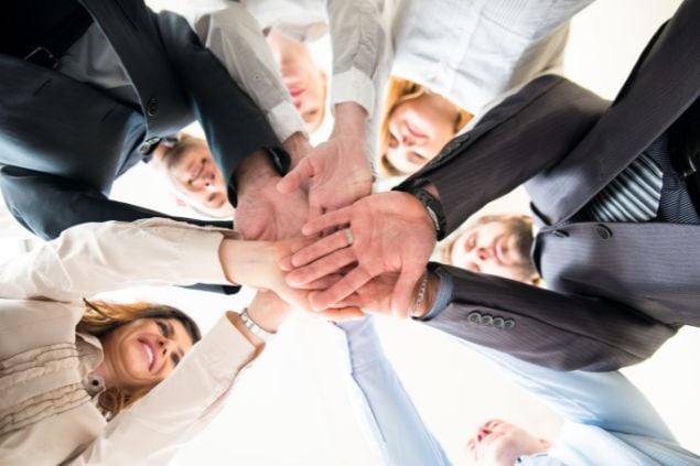 Imagem de um grupo de funcionários com as mãos uma em cima da outra em sinal de união