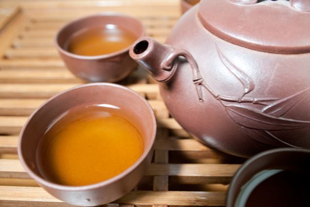 Imagem de duas xícaras de chá e uma chaleira do lado delas à mesa