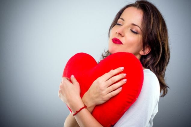 Imagem de uma mulher com os olhos fechados e abraçando um coração que parece ser de pelúcia