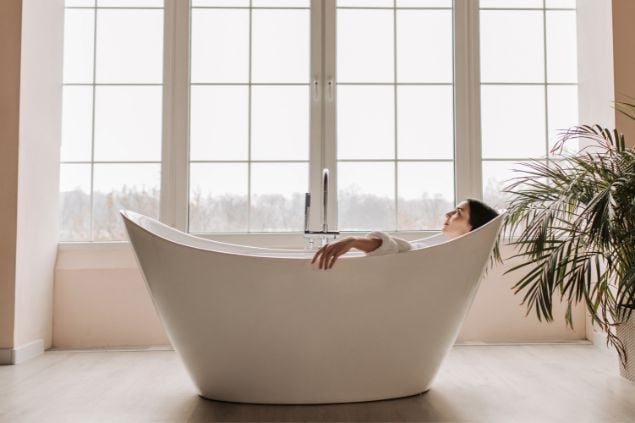 Imagem de uma mulher deitada em uma banheira, olhando para cima com feição de satisfação