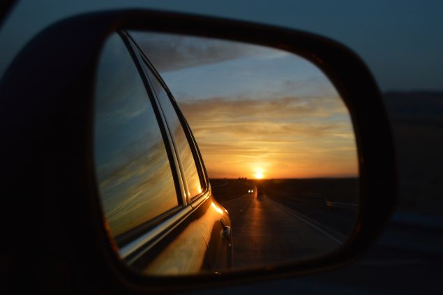 Imagem dos espelhos laterais do carro refletindo o pôr-do-sol e o carro seguindo em frente na estrada