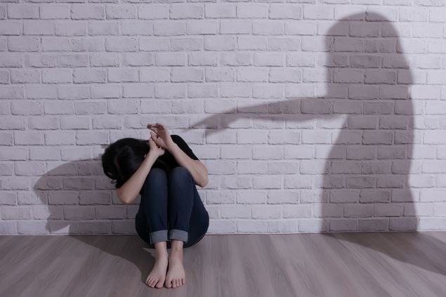 Imagem de uma pessoa acuada no chão e a parede a sombra de outra pessoa apontando para a primeira como se estivesse a orpimindo