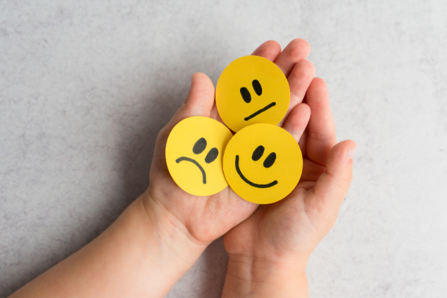 Pessoa segurando três desenhos de emoji: um triste, um feliz e outro indiferente 
