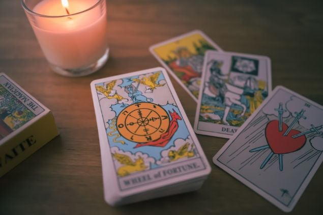 Imagem de uma mesa e sobre ela algumas cartas de tarot. Ao lado uma vela acesa.