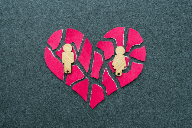  Conceito de divórcio, de término de relacionamento. Um coração de papel com dois bonequinhos, representando um casal, está repartido e rasgado. 