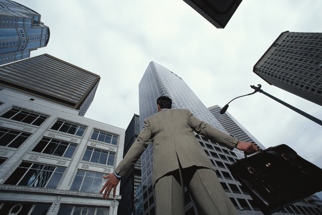 Homem perdido em uma cidade grande, olhando para os prédios de baixo para cima. 