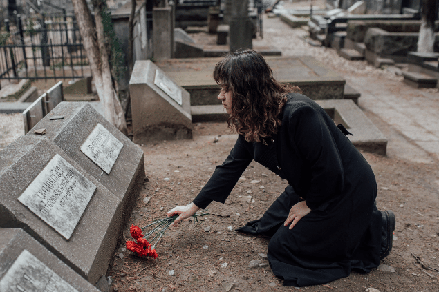 Mulher em um vestido preto oferecendo uma rosa em túmulo. 