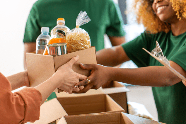 Voluntários entregando caixa com alimentos perecíveis em centro de assistência para refugiados. 