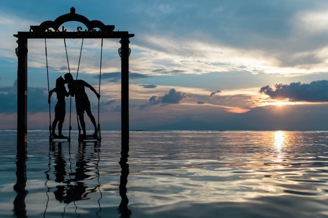 Homem e mulher em pé em balanços se beijando na praia.