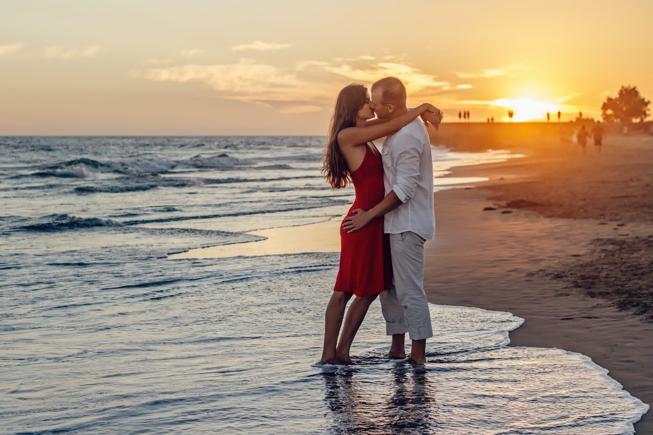 Homem e mulher, em praia, se beijando durante o pôr-do-sol.