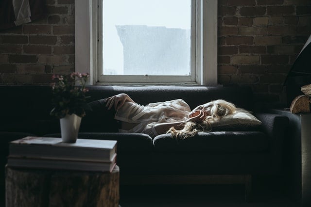 Mulher branca deitada num sofá cinza.