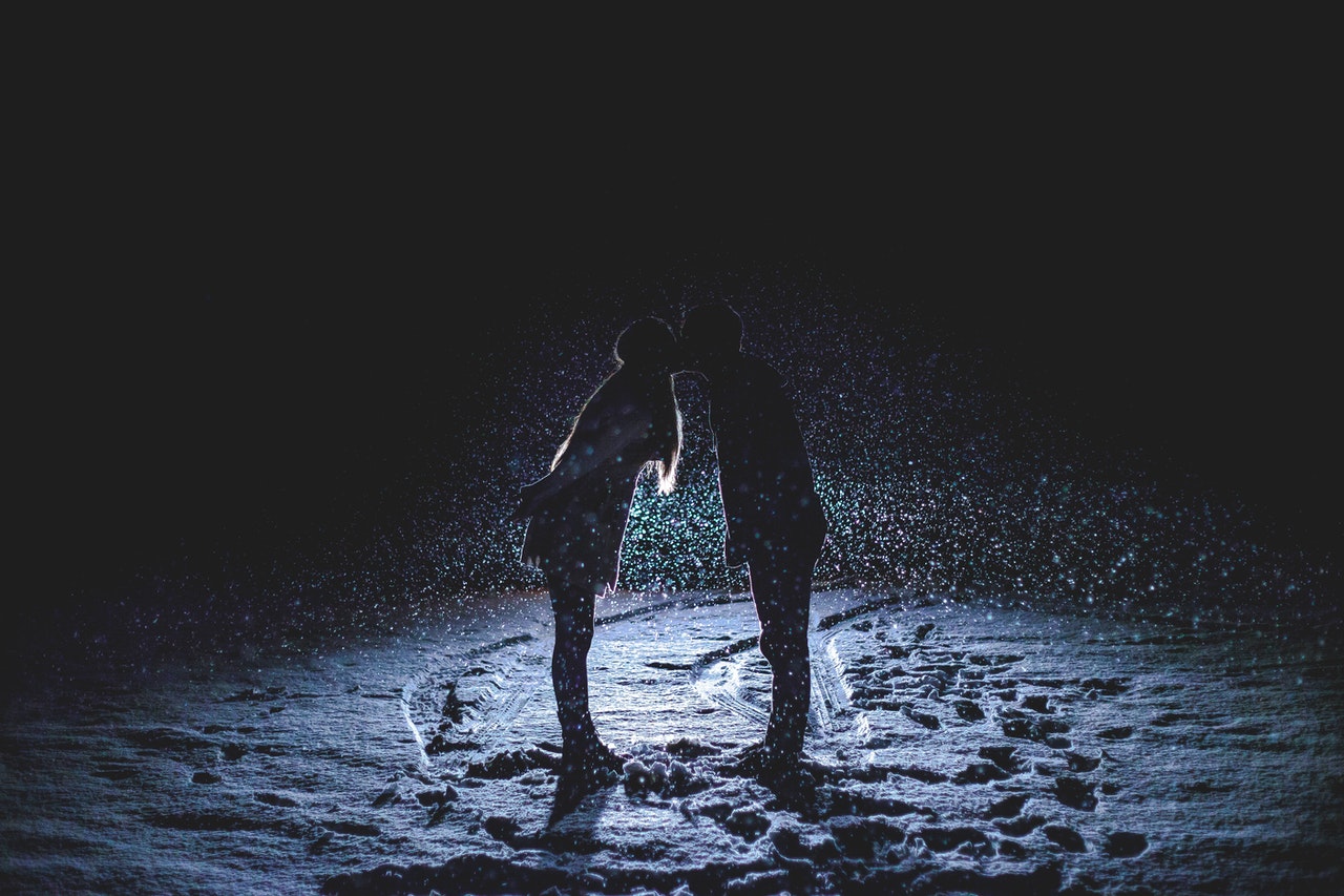 Silhueta de homem e mulher, de pé, na neve, se beijando.