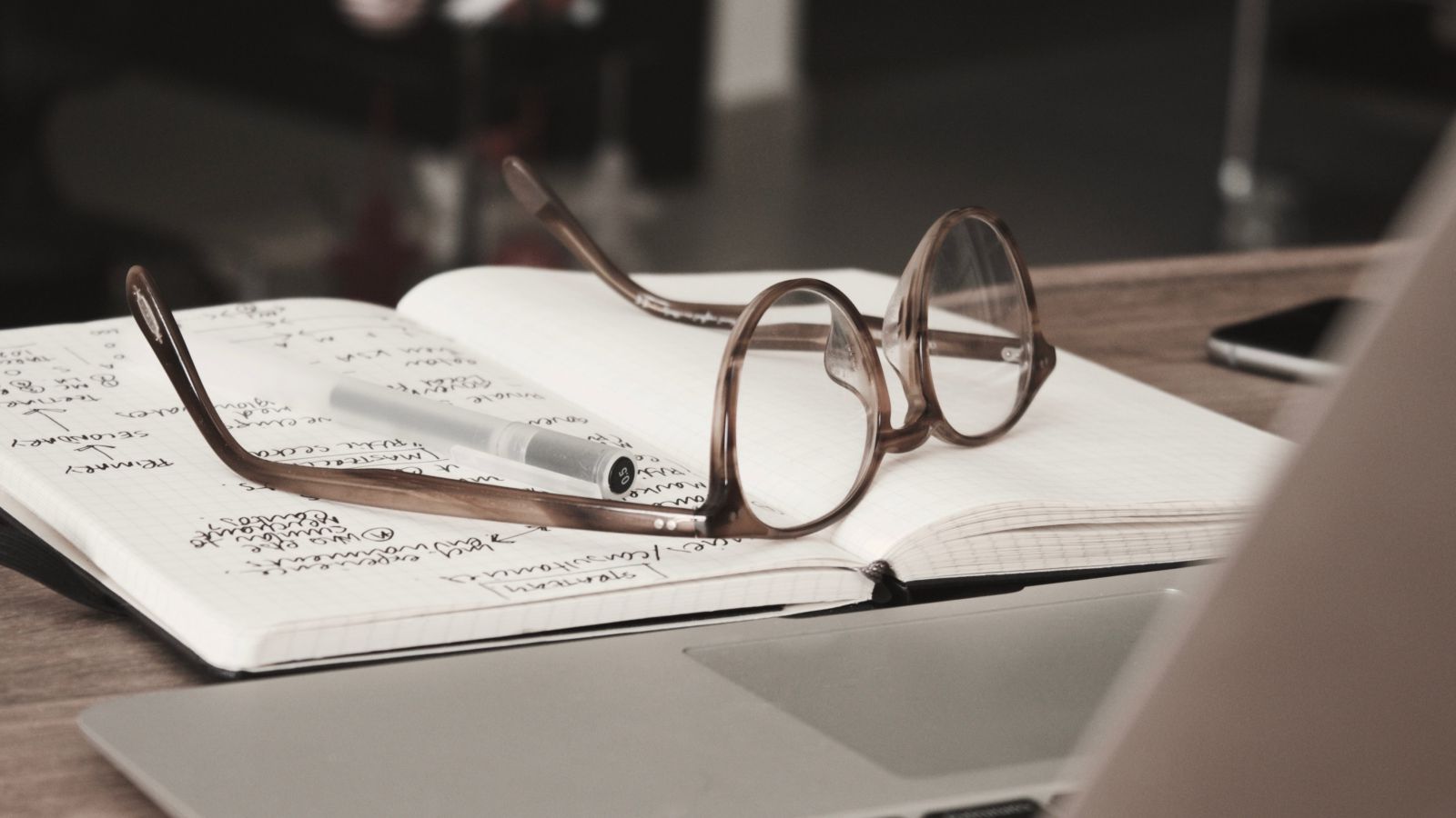 Caderno com escritos e óculos de grau sobre uma mesa de madeira