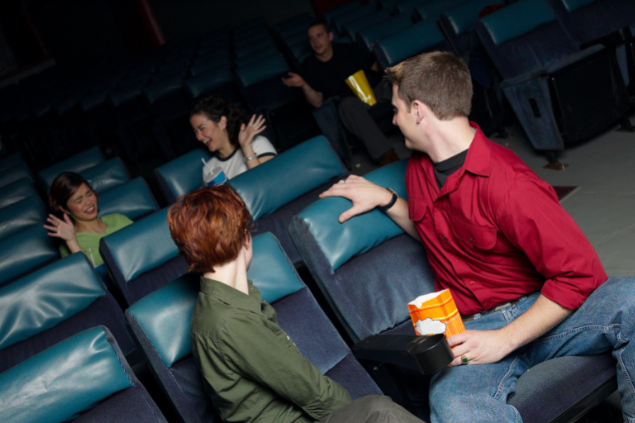 Homem bravo com duas mulheres conversando e rindo na sala de cinema
