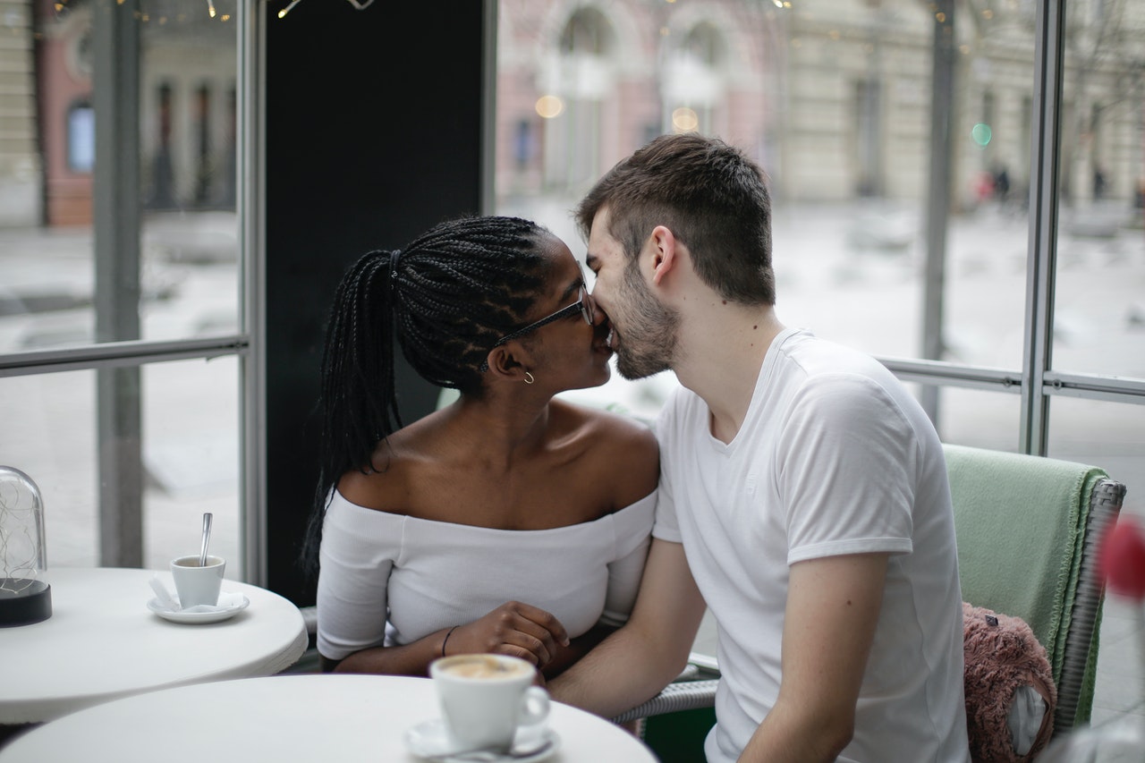 Homem e mulher, em um café, se beijando.