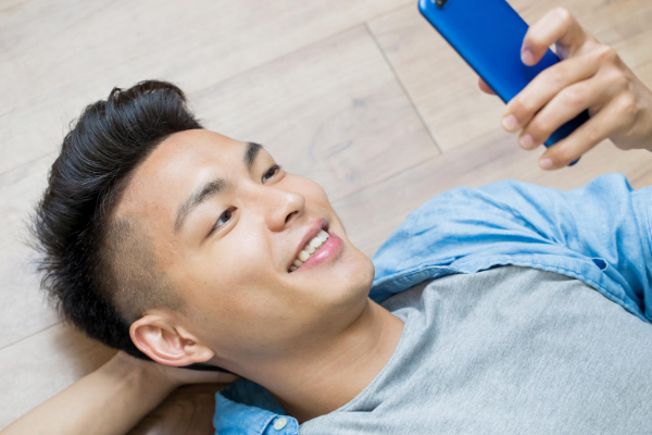 Homem deitado no chão, sorrindo, enquanto usa o telefone celular.