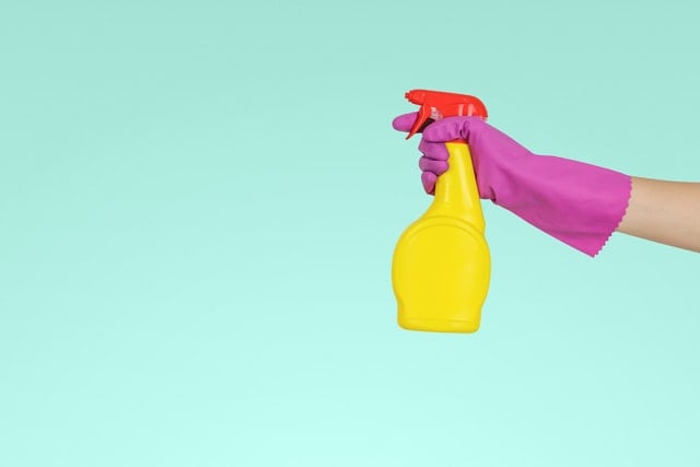 Mão com luva roxa segurando spray de embalagem amarela e tampa vermelha.