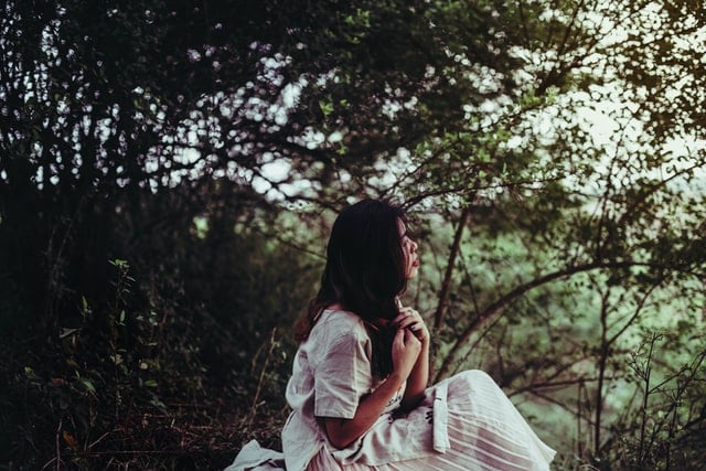 Mulher branca sentada no meio da floresta.
