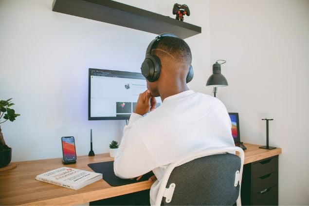 Homem em frente a uma tela de computador, trabalhando com fones de ouvido.
