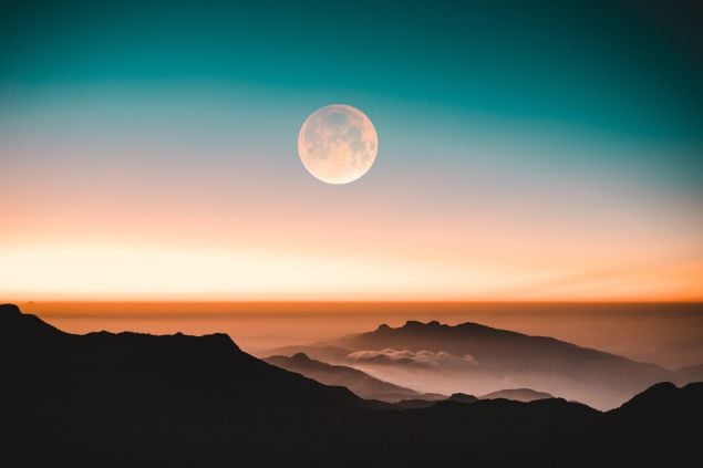 Lua cheia ao longe, em uma paisagem montanhosa.