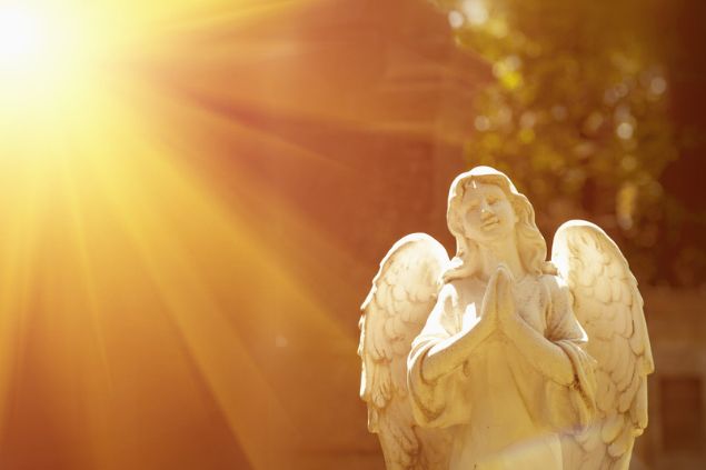 Estátua de um anjo orando e sorrindo, iluminado pelo Sol.