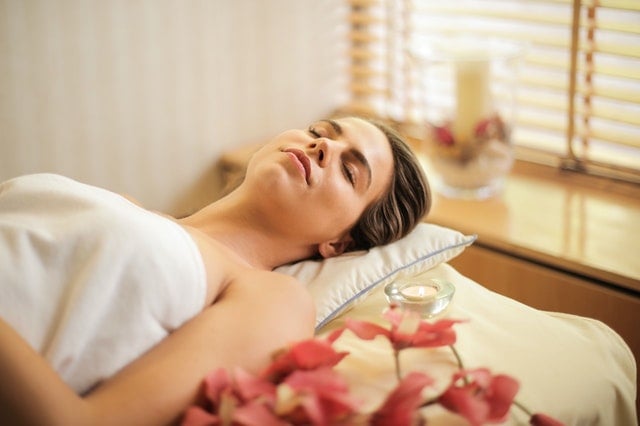 Mulher branca deitada numa maca de massagem, com vela branca acesa ao lado.