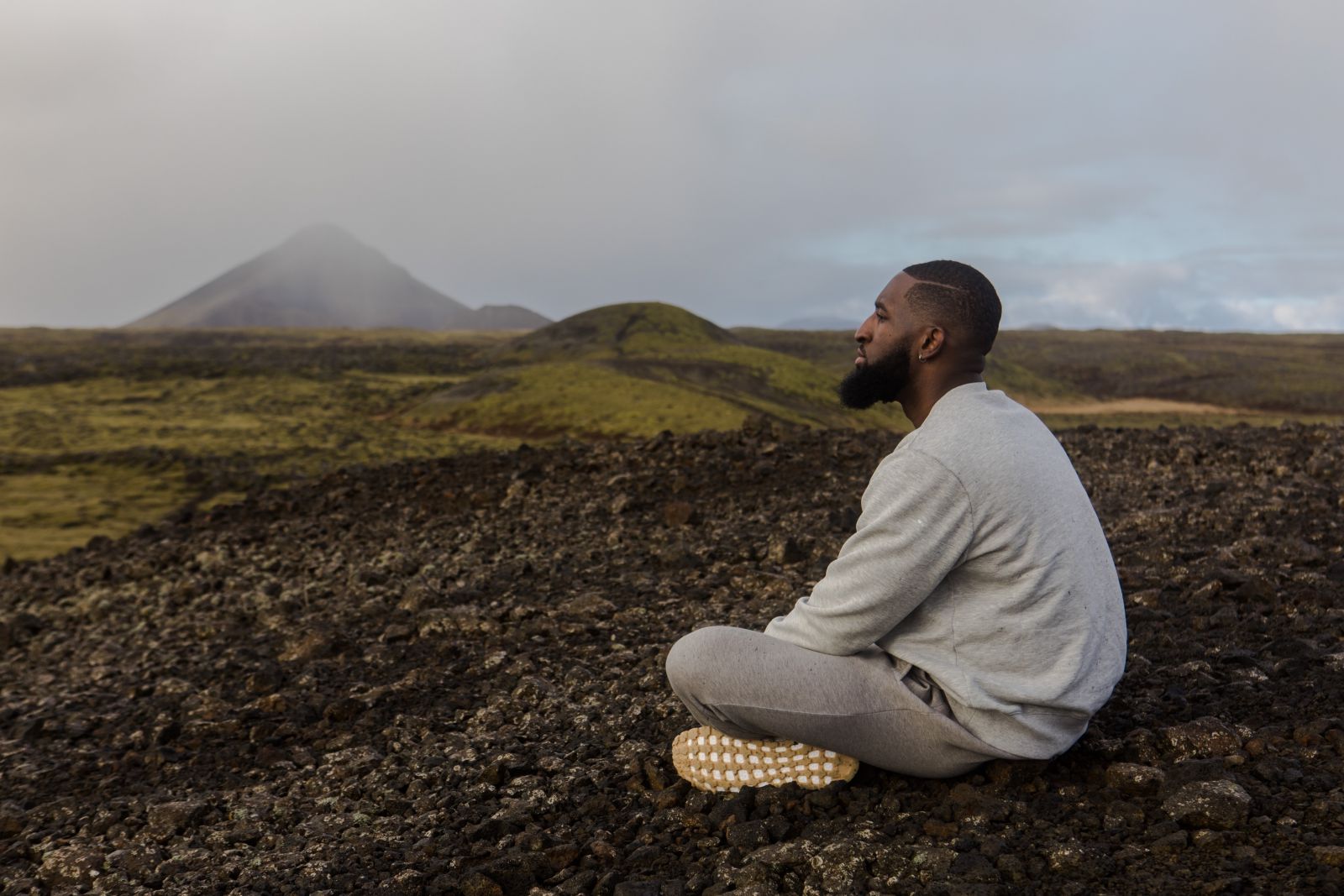 Homem sentado em uma local com terra e montanhas