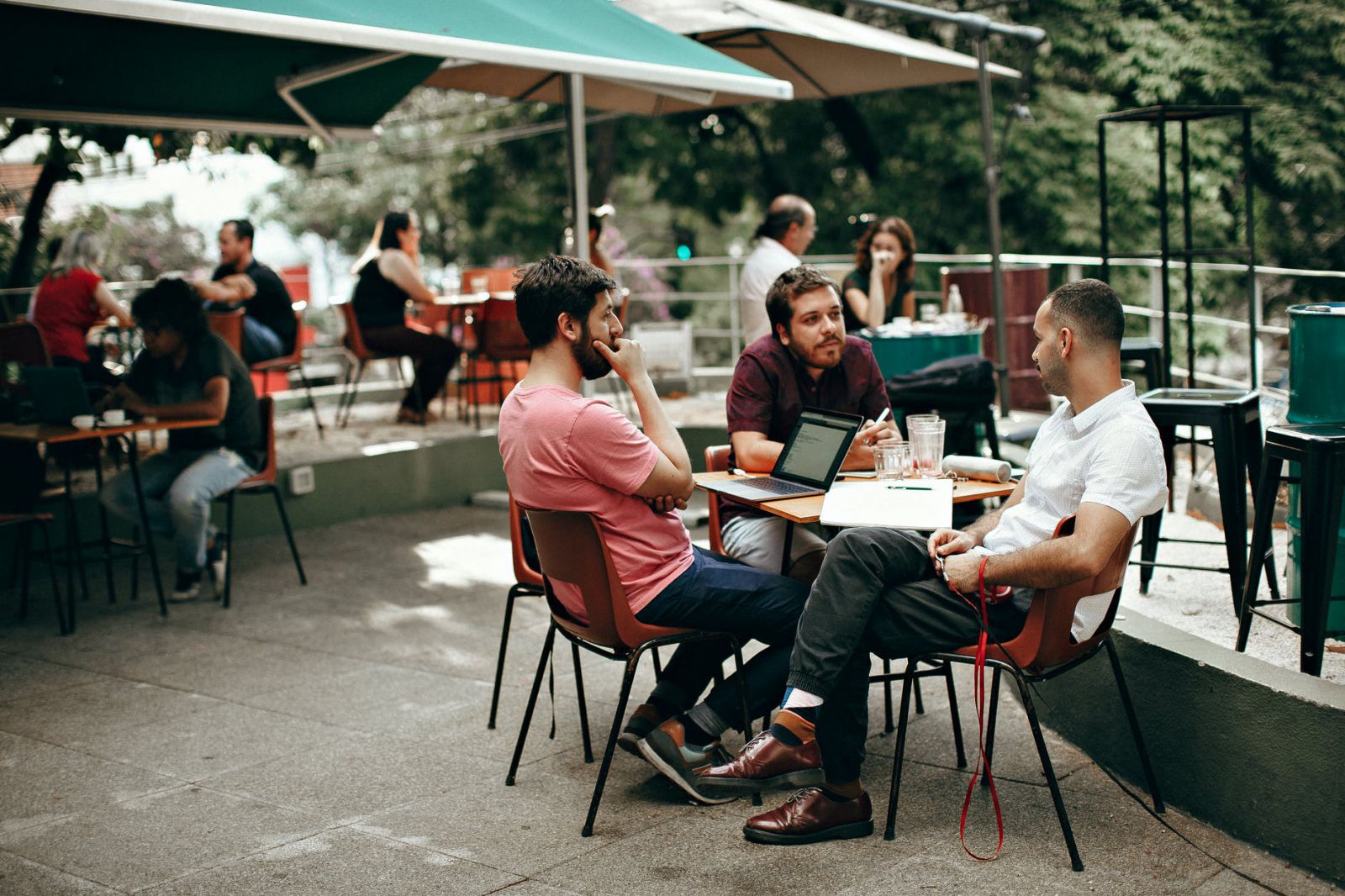 Grupo de homens brancos conversando numa mesa ao ar livre.