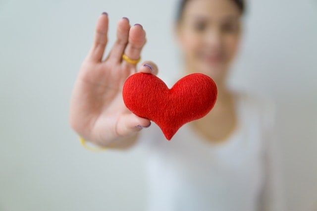 A mão de uma mulher segurando um coração de feltro