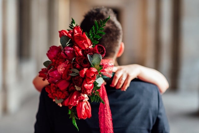 Mulher segura um buquê de flores enquanto abraça homem.