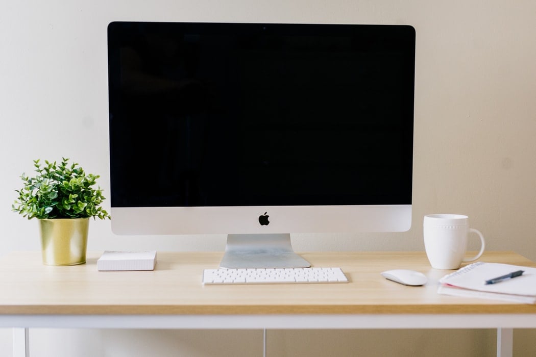 Mesa de trabalho minimalista com computador, planta, caneca e caderno.