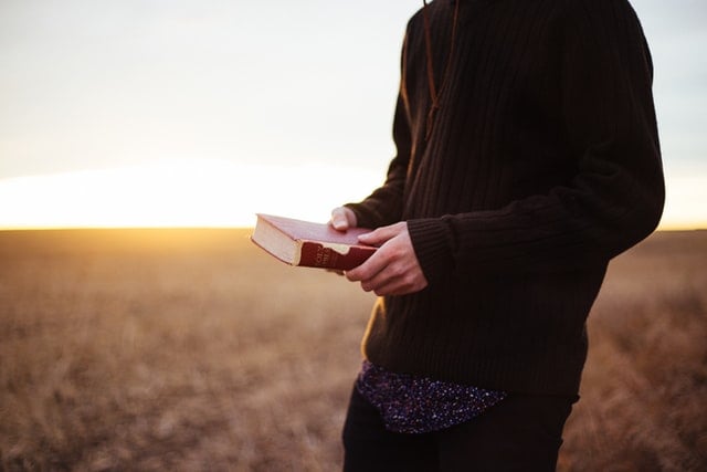 Homem branco segurando bíblia num campo.