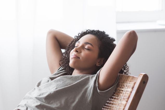 Imagem de uma mulher com os olhos fechados deitada e com feiçao de relaxamento