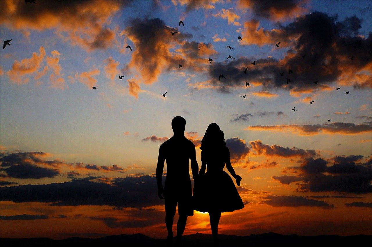 Silhuetas de homem e mulher andando de mãos dadas durante pôr-do-sol.