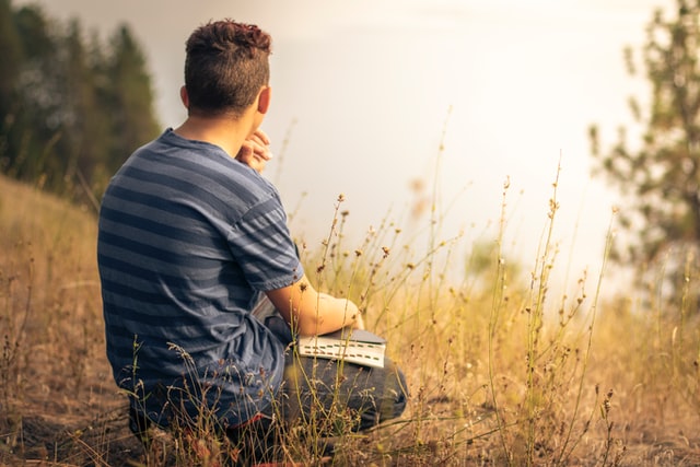 Homem branco sentado num campo com bíblia no colo.
